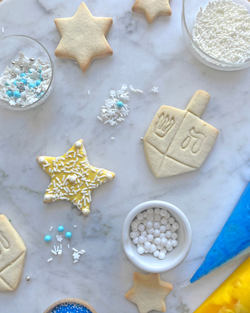 Dreidle Cookies, Dreidel Cookies, Star of David Cookies, and Star Cookies, with royal icing and sprinkles for a Hanukkah Cookie Decorating Kit.